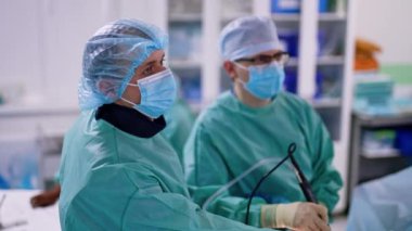 X-ray koruyucu tasma takan üniformalı erkek doktor, aletleri kullanarak ana cerrahın yanında duruyor. İki doktor laparoskopi yapıyor..