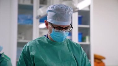 Şapkalı, maskeli ve gözlüklü bir cerrah hastaya bakıyor. Operasyon odasında çalışan bir doktorun portresi..