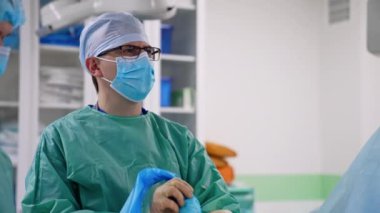 Gözlüklü yetişkin bir erkek cerrah laparoskopik bir alet tutuyor ve monitöre bakıyor. Doktora yardım ediyorum..