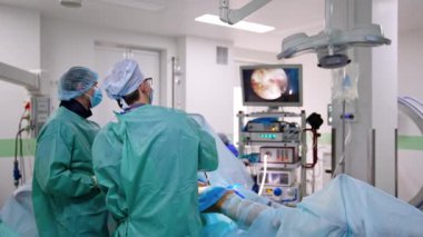 İki erkek cerrah ameliyathanede işbirliği yapıyor. Doktorlar modern cihazları çalışır durumda ve monitörü izliyorlar.
