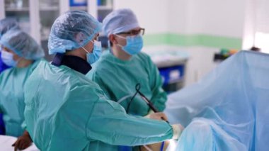 Üniformalı doktorlar laparoskopik ameliyat yaparlar. Cerrahlar prosedürü kontrol etmek için monitöre dikkatlice bakarlar..