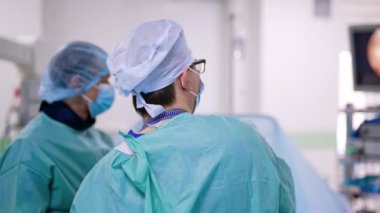 Ameliyatta meşgul olan bir cerrahın arka görüntüsü. Doktor bir cihaz kullanır ve monitördeki çalışmalarına bakar.