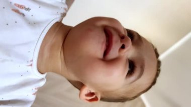 Kafkasyalı güzel bir çocuğun güzel yüzü. Küçük çocuk kameranın sağa sola eğilmesine bakıyor. Kapatın. Dikey görünüm.