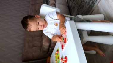 Masada oturan beyaz, şirin bir çocuk var. Bir oyuncakla oynayan sevimli bir bebek. Çocuk oyuna odaklanmış. Dikey görünüm.