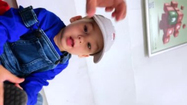 Süveter, kot pantolon ve şapka içinde güzel bir bebek. Sevimli bir erkek bebeğin portresi. Kapatın. Dikey görünüm.