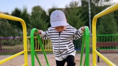 Sevimli erkek bebek kaydırağa tırmanıyor. Neşeli, mutlu, beyaz bir çocuk aşağı kayıyor. Oyun parkında geçen süre.