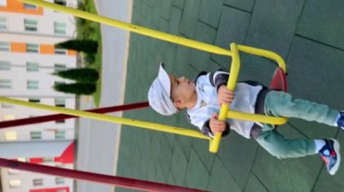 Sakin bir oğlan dışarıda salıncakta sallanıyor. Şapkalı bir çocuk sallanıyor ve yana bakıyor. Dikey görünüm.