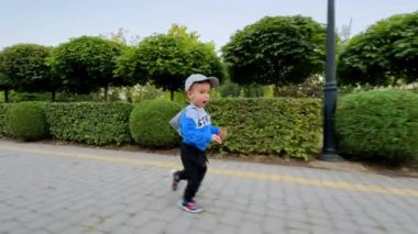 Spor takım elbiseli ve parkta şapka takan aktif bir çocuk. Bebek dışarıda iyi vakit geçiriyor..
