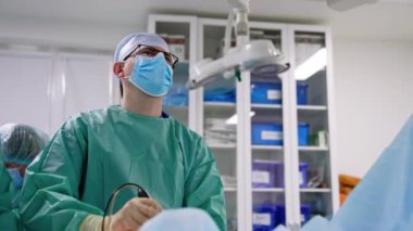 Gözlük takan ve monitöre bakan kendinden emin bir erkek cerrah. Doktor laparoskopik aygıt tutuyor. Düşük açı görünümü.