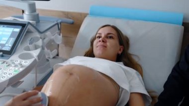Güzel, beyaz, hamile kadın ultrason yaptırırken yalan söylüyor. Doktorun son aşamalardaki hamilelik incelemesi.