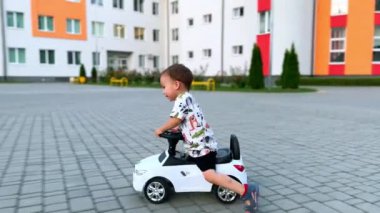 Asfalt yolda oyuncak arabasıyla gezen küçük mutlu çocuk. Aktif erkek bebek yerden hızla yükseliyor..