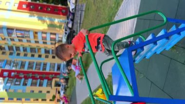 Sevimli gülümseyen bebek kaydırağa tırman. Beyaz tenli şirin bir çocuk oyun parkında kayıyor. Dikey ekran.