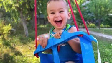 Heyecanlı beyaz erkek bebek salıncakta neşeli sallanıyor. Mutlu çocuk yazın bahçede eğleniyor..