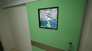 Kocaman açık yeşil bir kapı ve kare bir pencere. Operasyonun yapıldığı modern bir ameliyathanenin kapıları kapalı..