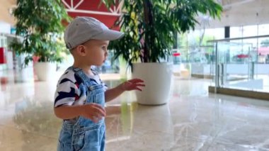 Şapkalı ve kot pantolonlu tatlı çocuk alışveriş merkezinde duruyor. Meraklı çocuk etrafta koşuşturuyor..