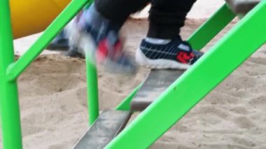 Küçük çocuğun ayakları merdivenlerden yukarı çıkıyor. Tanınmayan çocuk oyun parkındaki basamakları tırmanıyor..