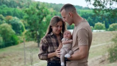 Yavru bebekleri dışarıda duran beyaz bir çift. Anne ve baba oğullarını rüzgardan koruyorlar. Anne bebeğin başını öper..