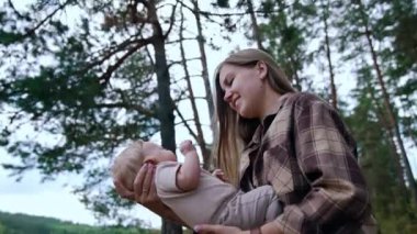 Anne, bebeğini önünde tutarak sallıyor. Kadın konuşur, bebeğine gülümser ve onu göğsüne bastırır..