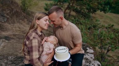 Bebek hayatının iki ayını kutluyoruz. Mutlu ebeveynler bir bebek kucaklar ve doğada otururlar..