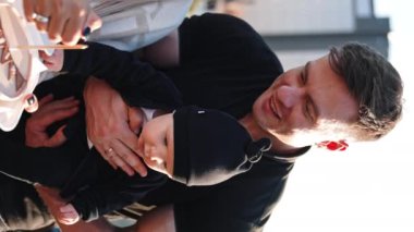 Elinde bebekle gülümseyen beyaz bir adam. Uzun saçlı kadın pastaya mum yakmaya çalışıyor. Dikey ekran.