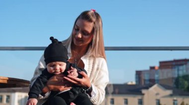 Güzel bebeğiyle uzun saçlı sarışın bir kadın. Siyah takım elbiseli küçük bebek ve güneş ışınlarında şapka.