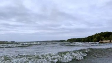 Hızlı dalgalar gölün kıyısına yaklaşıyor. Suyun üstündeki gökyüzü gri bulutlarla kaplıdır. Kasvetli yaz günü görüntüleri.