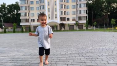 Tişört giyip kameraya doğru koşan sevimli beyaz çocuk. Sevimli bebek kameraya dokunup kaçıyor..
