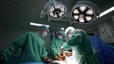 Ayak travmasını cerrahi ekip yönetiyor. Erkek doktor, ameliyat yerini aydınlatmak için yuvarlak lambayı çeker. Düşük açı görünümü.
