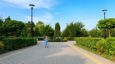 Asfalt yolda mutlu adımlarla yürüyen kot giyen sevimli çocuk. Şirin gülümseyen çocuk kameraya doğru koşuyor. Bebek parkta yürüyor..