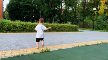 Çıplak ayaklı bir çocuk dışarıda koşuyor. Parkta kaçan tişörtlü ve şortlu bir çocuk..