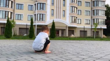 Yürüyen çocuğun kaldırımlı yolda çömelmiş tuğlalara dokunuşunun arka görüntüsü. Çocuk ayağa kalkar, koşar ve tekrar oturur..