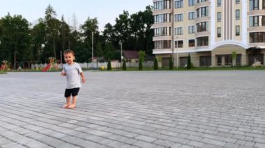 Beyaz tenli güzel çocuk dışarıda yalınayak yürüyor. Çocuk kameraya bakar, konuşur ve gülümser..