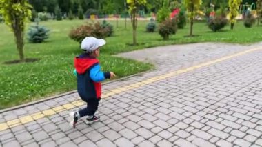 Parkta koşan ceketli, şapkalı ve pantolonlu mutlu çocuk. Neşeli çocuğun dışarıda aktif zaman geçirmesini izlemek..