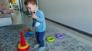 Şirin beyaz bebek oyuncak piramidi monte ediyor. Küçük çocuk evde oyuncaklarıyla oynuyor..