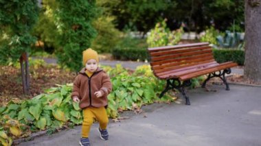 Sarı takım elbiseli, kepli ve kahverengi ceketli çocuk yolda. Aktif çocuk bir kestane almak için banka koşar..