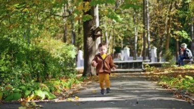 Kahverengi ceketli sevimli beyaz erkek bebek parkın önünden geçiyor. Tatlı çocuk sabun köpüklerine ilgiyle bakıyor..