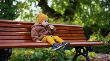 Sonbaharda bankta oturan küçük bebek. Bebek çocuk ağzında paketle meyve püresi yiyor..