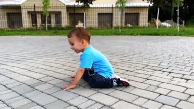 Asfalt zeminde oturmuş neşeli, enerjik bir çocuk. Bebek yerde sürünüyor ve ayağa kalkıyor..