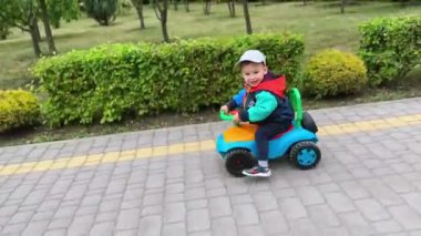 Dışarıdaki oyuncak arabaya binen ceketli ve şapkalı neşeli beyaz çocuk. Parkta yürürken mutlu aktif çocuk.