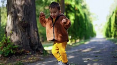 Enerjik neşeli Kafkasyalı çocuk dışarıda mutlu bir şekilde zıplıyor. Parkta yürüyen tatlı erkek bebek..