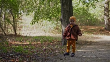 Sarı şapkalı, takım elbiseli ve ceketli sevimli çocuk parkta yürüyor. Küçük çocuk bir parmağıyla yukarıya doğru koşuyor..