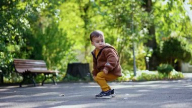 Beyaz çocuk kahverengi ceket giyip sabun köpüğü yakalıyor. Bebek parkta yürüyüş yaparken eğleniyor..