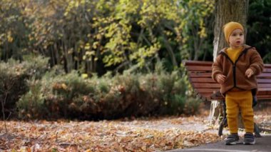 Sarı takım elbiseli, şapkalı ve ceketli çocuk parkta duruyor. Çocuk etrafına bakıyor ve sonra kameraya geliyor..
