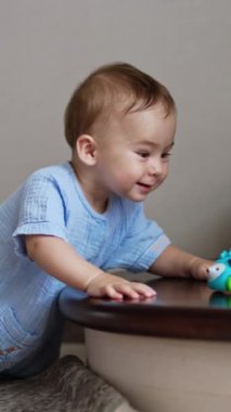 Evin içinde merdivenlerin yanında dizlerinin üzerinde duran mutlu gülen çocuk. Sevimli çocuk oyuncağa bakar ve neşeyle sallanır. Dikey video