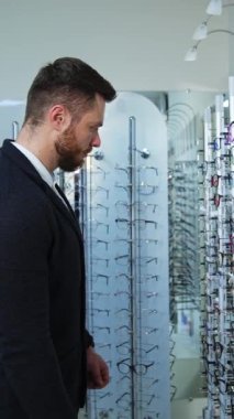 Gözlük mağazasında erkek müşteri. Dükkanda gözlük seçen yakışıklı bir adamın profil görüntüsü. Optik alıcısı. Dikey video
