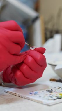 Laboratuvar çalışanı göz protezi boyuyor. Klinikte fırçayla yapay göz yapan kırmızı lateks eldivenler ustası. Yakın plan. Dikey video