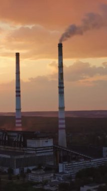 Kırsal kesimde zararlı bir fabrika. Gece gökyüzünde batan güneşli kule boruları olan endüstri. Üretimden çıkan kimyasal duman havayı kirletir. Yukarıdan bak. Dikey video