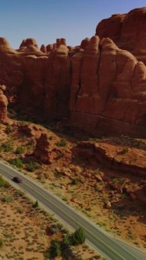 Otobanda hareket eden arabalar garip şekilli turuncu kayalar boyunca ilerliyorlar. Utah, ABD 'deki Arches Ulusal Parkı' nın harika kanyonları. Dikey video