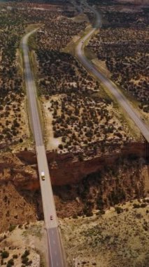 Utah Ulusal Parkı 'nın ıssız topraklarında büyük bir hendek. Hendeğin kenarlarını hareket halindeki arabalarla birleştiren iki köprü. Hava görüntüsü. Dikey video