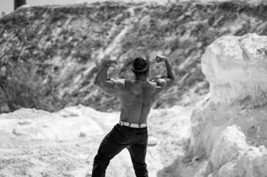 Rocky Peyzaj 'da Kaslı Adam. Kaslı bir adam kaslı bir arazide kaslarını esnetir, fiziğini ve gücünü gösterir..